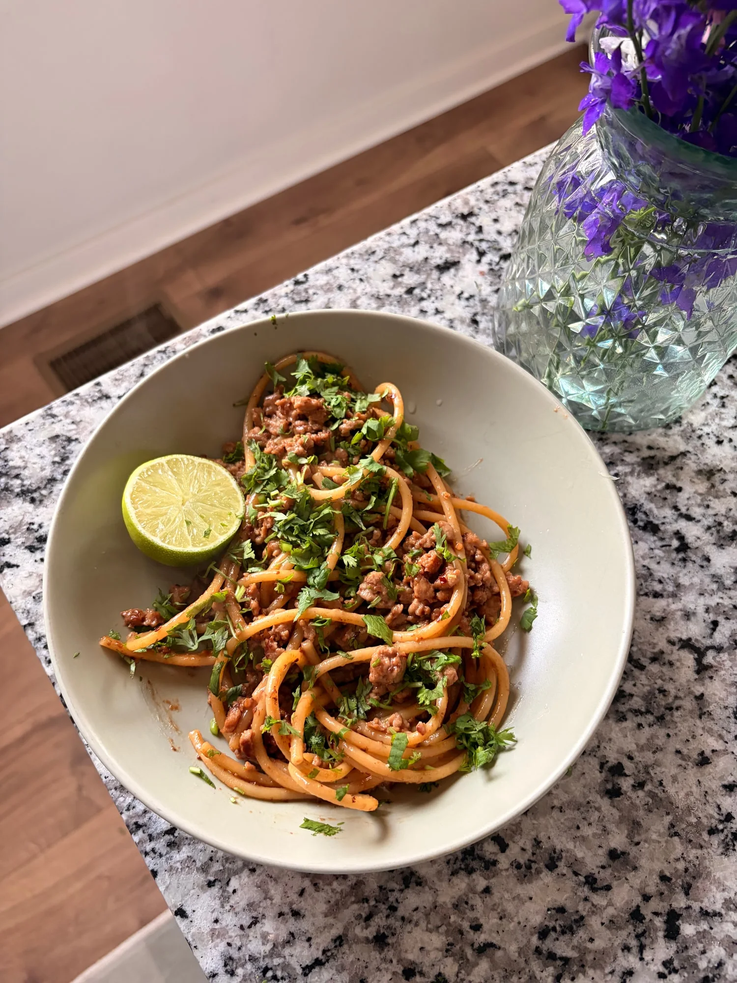 Thai peanut turkey pasta with cilantro and a lime half, purple flowers beside the bowl